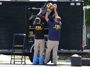 caption: FBI officials unload the equipment as they process the home of Craig Robertson who was shot and killed by the FBI in a raid on his home this morning on August 9 in Provo, Utah.