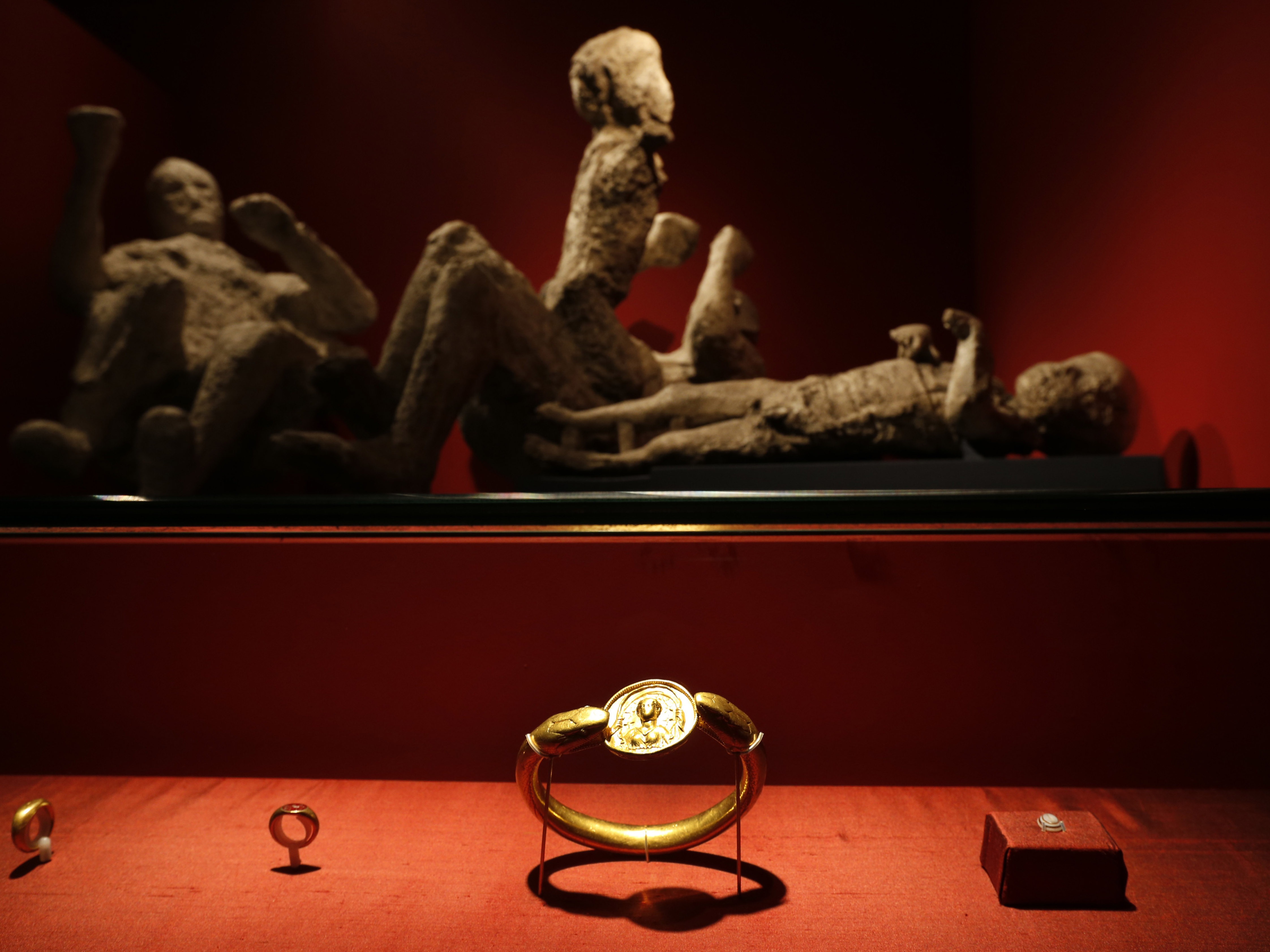 caption: Jewelry found in the ruins of a house in Pompeii are displayed, backdropped by the casts of two adults and two children who died together, are seen housed at the British Museum in London in 2013.