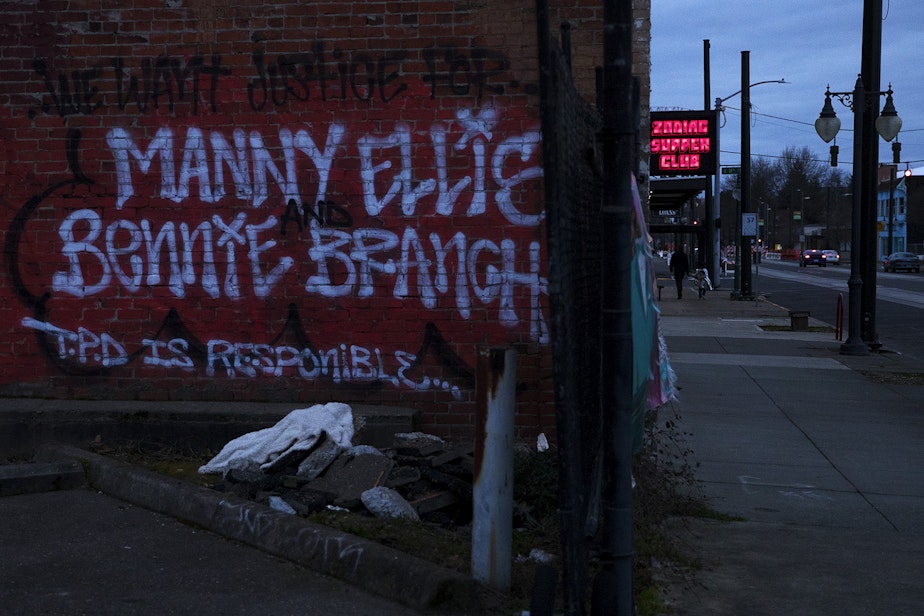 caption: 'We want justice for Manny Ellis and Bennie Branch. T.P.D is responsible," is shown spray painted on a brick wall along Martin Luther King Jr. Way, after a silent march honoring 33-year-old Manuel Ellis, who was killed by Tacoma police on Sunday, Feb. 28, 2021, in Tacoma. 