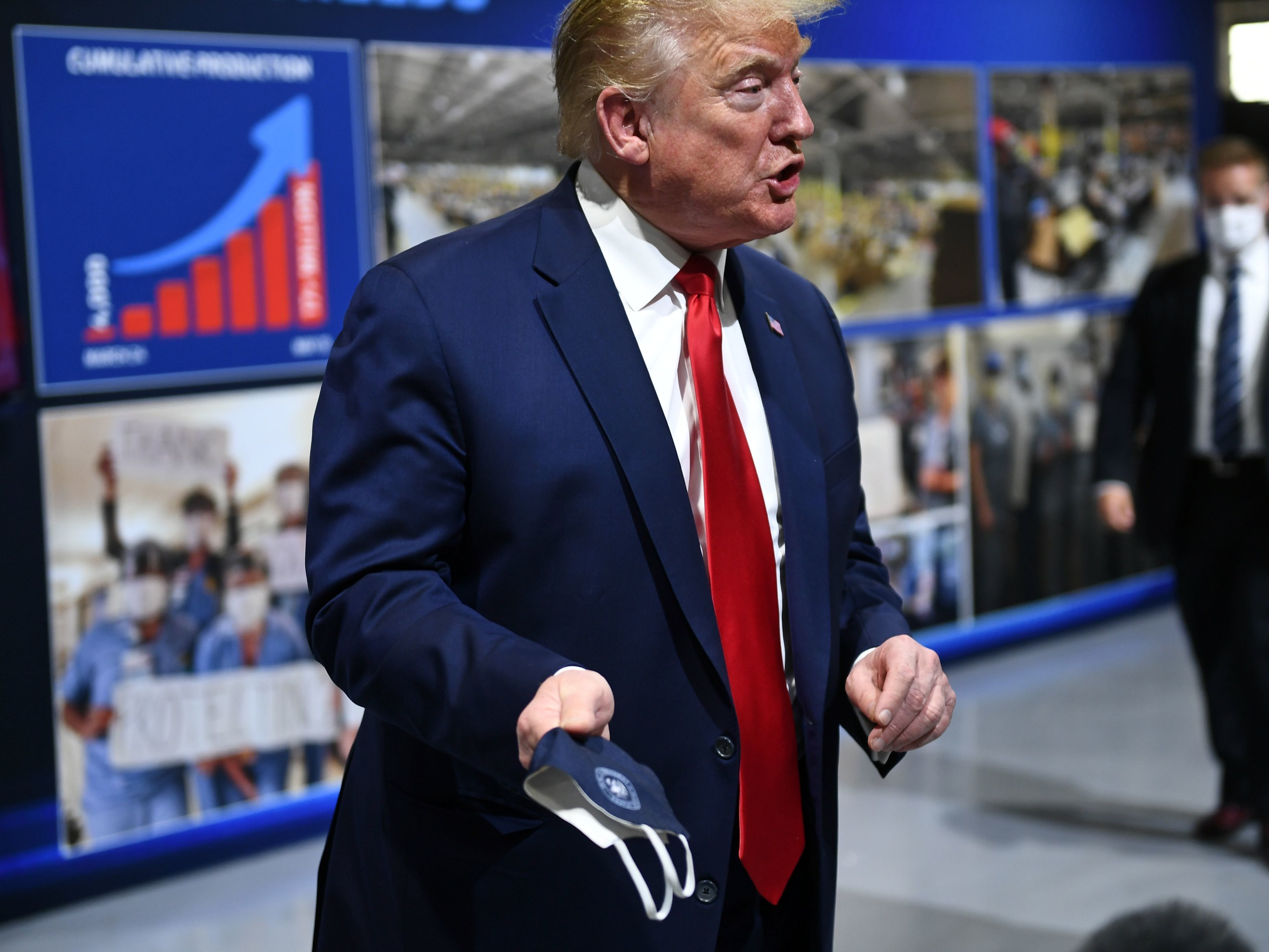 caption: President Trump holds a mask as he speaks during a tour of the Ford Rawsonville Plant in Ypsilanti, Mich., Thursday.
