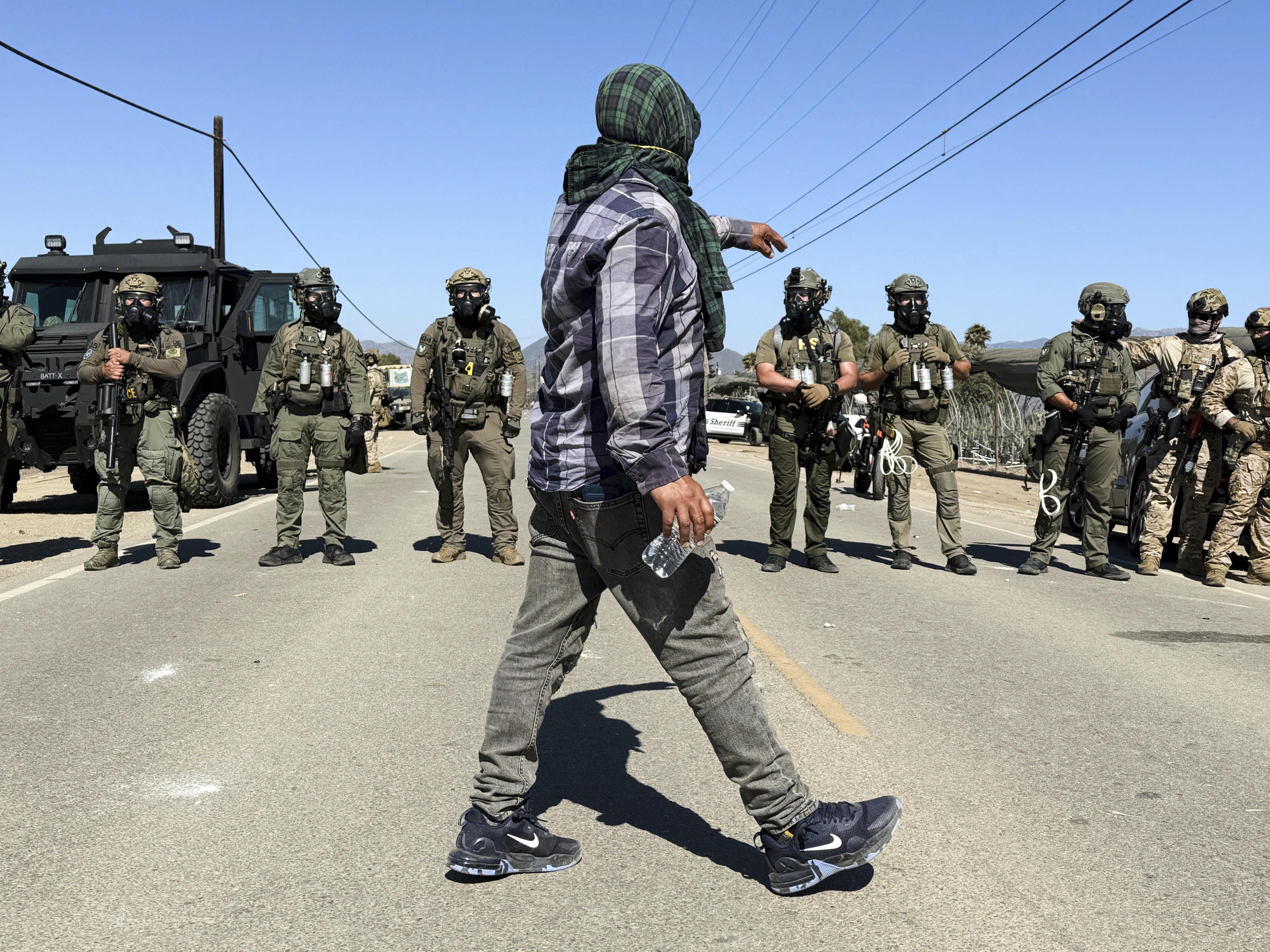 caption: A demonstrator walks in front of federal agents blocking a road during an immigration raid in Camarillo, Calif., Thursday, July 10, 2025.