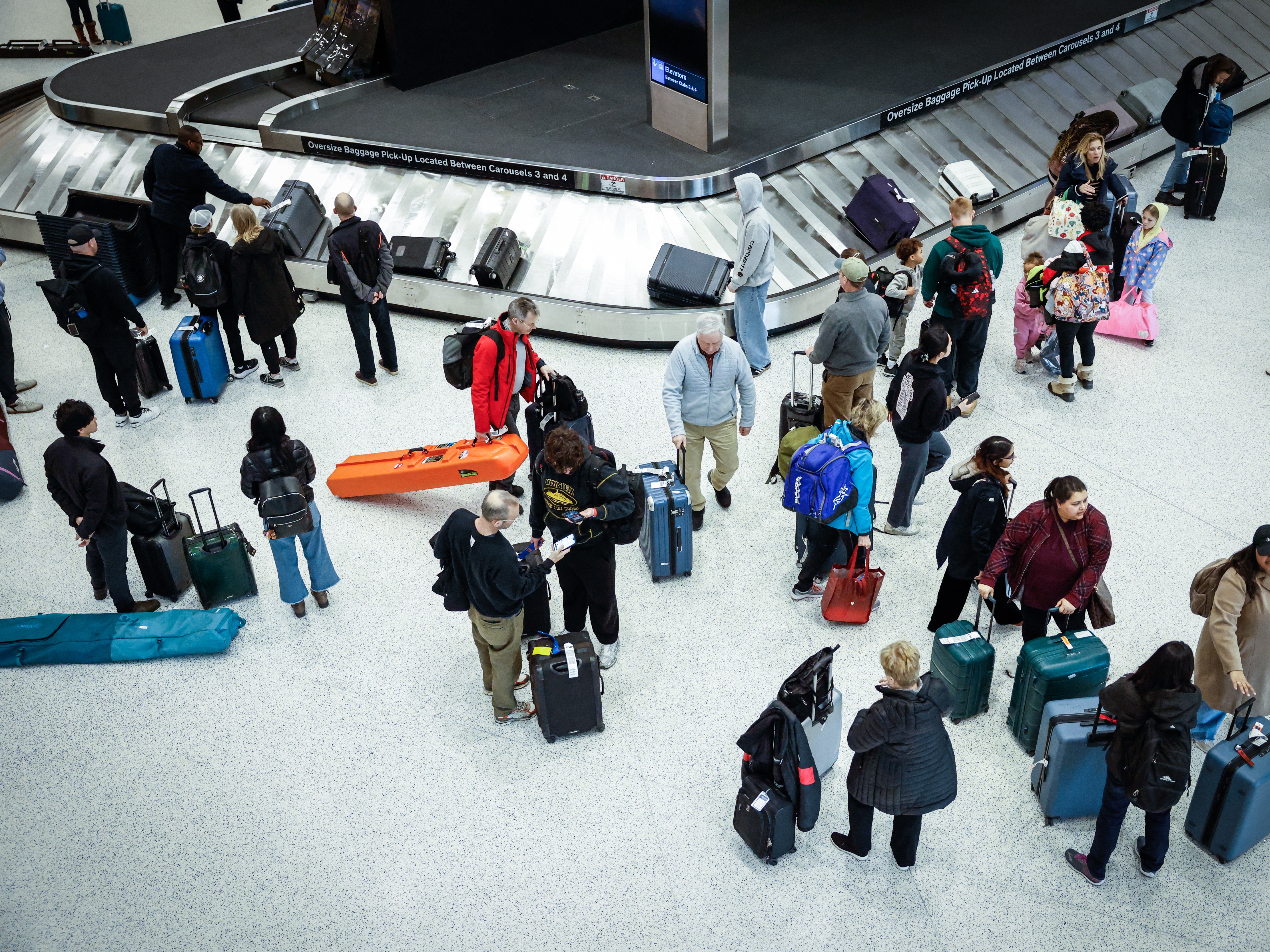 caption: Travelers gather at baggage claim station at Newark International Airport in Newark in March. Some passengers may be newly incentivized to stick to a carry-on as airlines increase checked bag fees.
