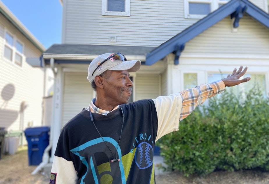 caption: Reginald Dennis, who has lived in the Central Area and Rainier Valley for most of his lifetime, waves to a passing friend in a car outside the rental home where he lives