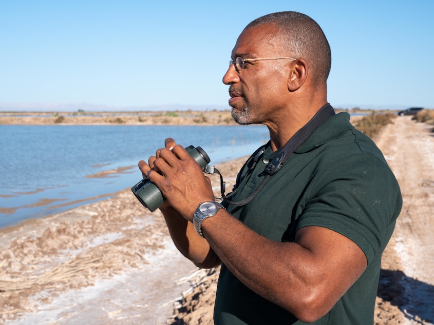 caption: Christian Cooper watches distant shorebirds at the Sonny Bono Salton Sea National Wildlife Refuge in California. The National Geographic channel has announced that Cooper will host a series called <em>Extraordinary Birder</em>. Cooper was in the spotlight after a woman in New York City's Central Park called the police and falsely accused him of threatening her in May 2020.