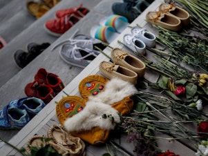 caption: Flowers, shoes and moccasins sit on the steps of the main entrance of the former Mohawk Institute, which was a residential school for Indigenous kids, in Brantford, Ontario. The memorial is to honor the children whose remains were discovered in unmarked graves in recent months in Canada.