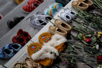 caption: Flowers, shoes and moccasins sit on the steps of the main entrance of the former Mohawk Institute, which was a residential school for Indigenous kids, in Brantford, Ontario. The memorial is to honor the children whose remains were discovered in unmarked graves in recent months in Canada.