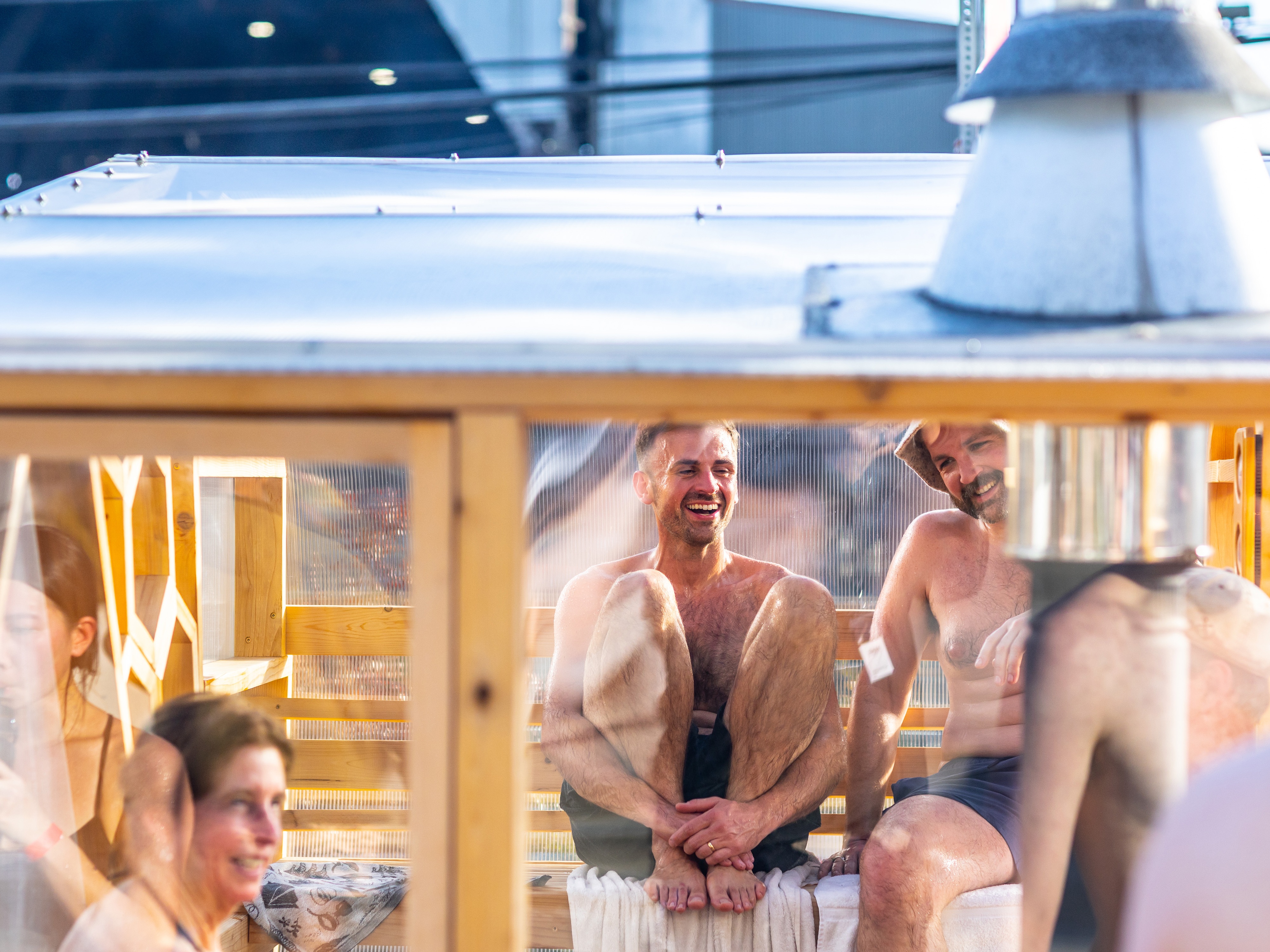 caption: Sauna enthusiast Michael Calcagno, second from right, sits inside a clear-walled wood-fired sauna during the Seattle Sauna Festival in November. Sauna use has taken off as a health practice and scientists are studying its benefits.