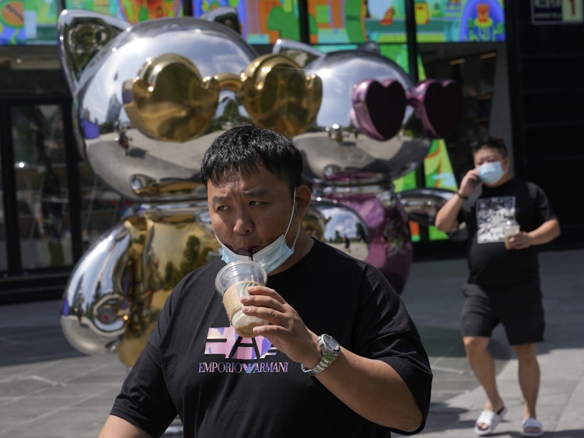 caption: A man lowers his mask to drink from a cup as he past near a mall, Wednesday, July 13, 2022, in Beijing.