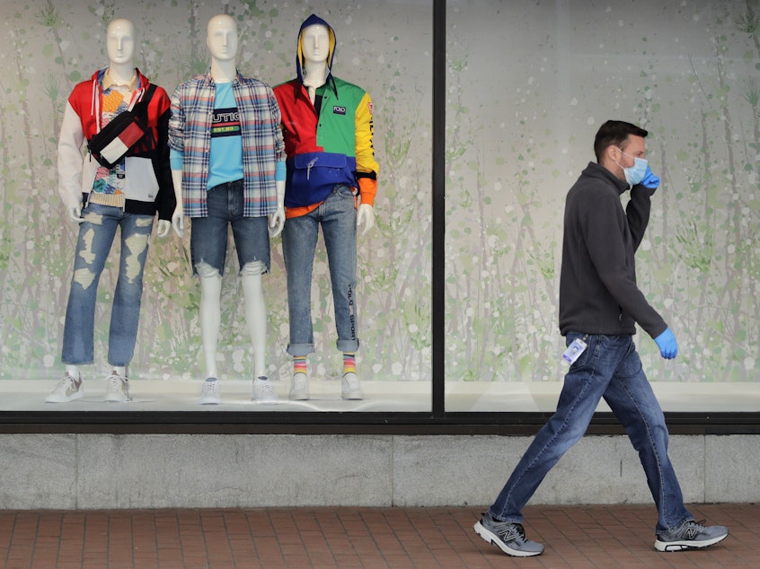 caption: A man walks past mannequins in the windows of a Macy's store in Boston on April 15. The company said its online sales started growing in April, but they "only partially offset" the losses from its stores.