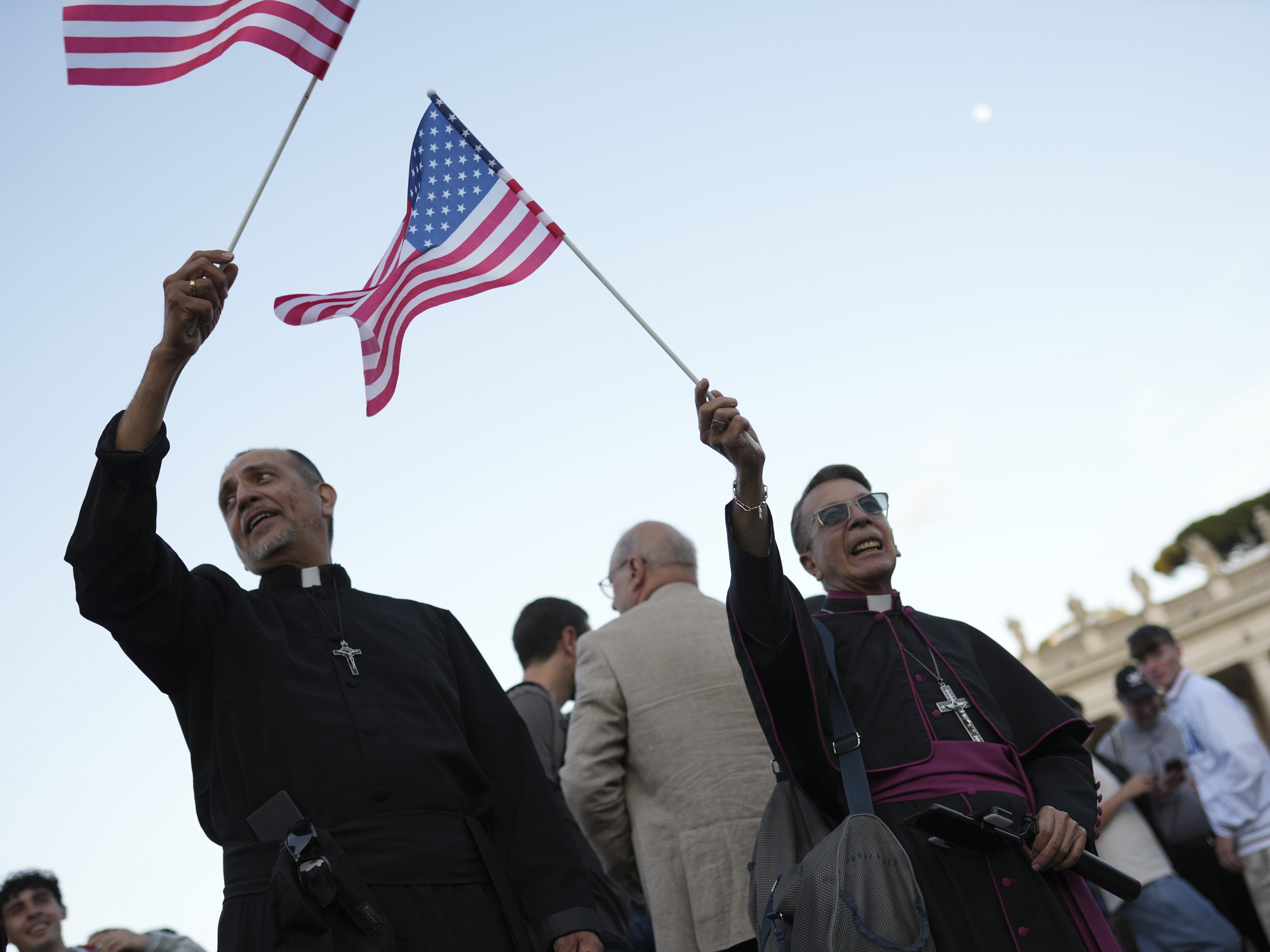 caption: Clerics wave US flags during the speech of the newly elected Pope Leo XIV at the Vatican, Thursday, May 8.
