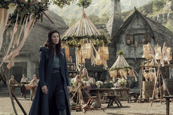caption: Moiraine (Rosamund Pike) visits a remote village in search of something — or someone — in Amazon's <em>The Wheel of Time</em>.