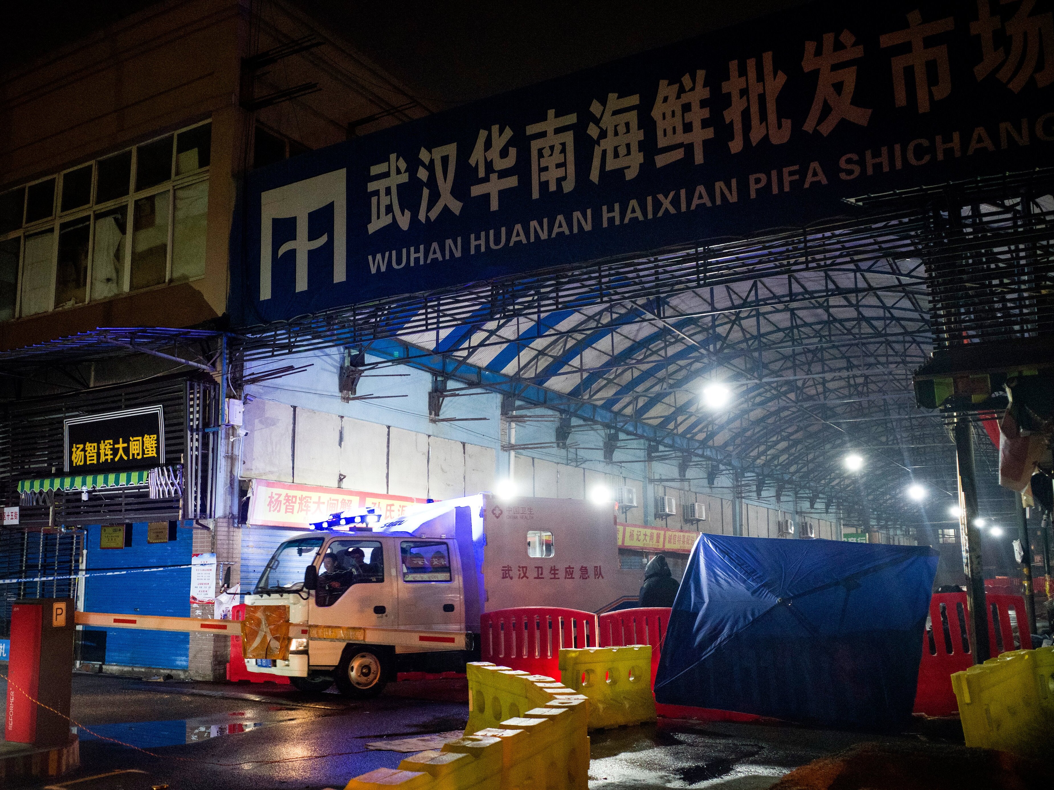 caption: A vehicle belonging to the Wuhan Hygiene Emergency Response Team drives past the shuttered Huanan Seafood Wholesale Market in Wuhan, China, on Jan. 11, 2020 — the day that the Wuhan health commission reported what is believed to be the first death from COVID-19. A new study points to raccoon dogs sold in the market as the likely source of the spillover of the SARS-CoV-2 virus from animals to humans.