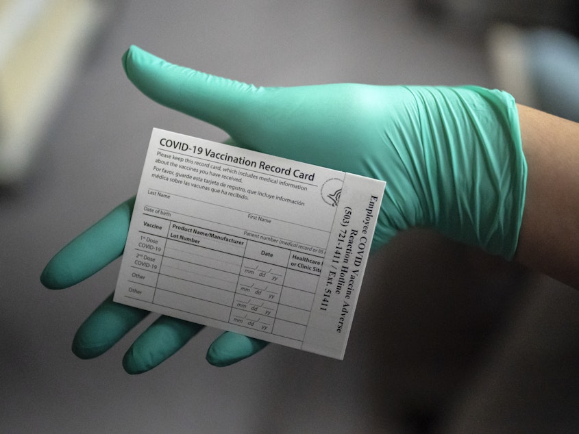 caption: A healthcare worker displays a COVID-19 vaccine record card at the Portland Veterans Affairs Medical Center in December.