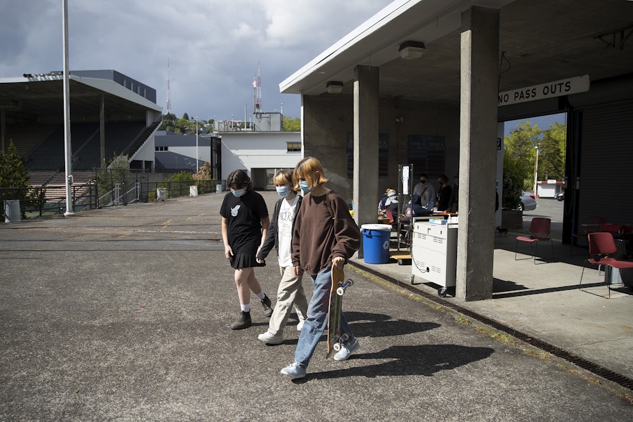 caption: Students at The Center School from left, Oskar, Dakota and Clem, walk toward the observation area after Clem, right, received a dose of the Pfizer Covid-19 vaccine from Seattle Fire Department Captain Melissa Woolsey, on Tuesday, May 18, 2021, at Memorial Stadium in Seattle.
