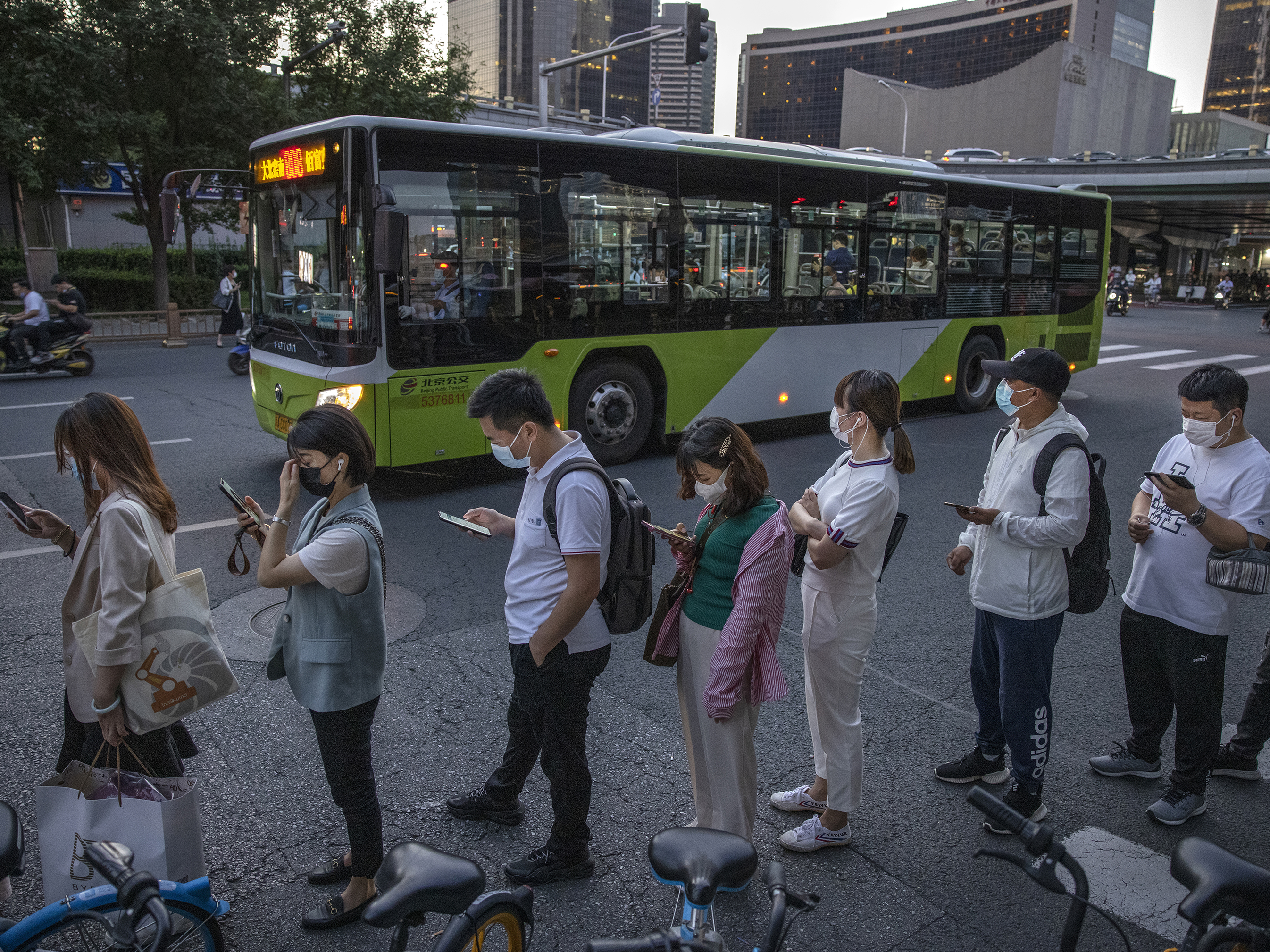 caption: Commuters wait in line for public buses as they leave work in Beijing's business district on Aug. 27. China's Supreme People's Court has ruled that it's illegal for companies to subject employees to the practice known as "996," or working 9 a.m. to 9 p.m. six days a week.