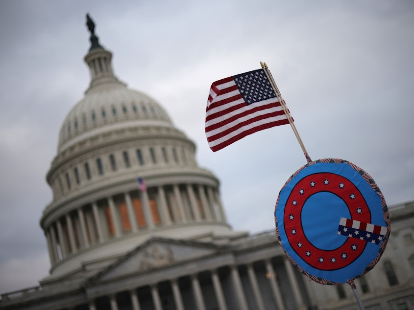 caption: Supporters of then-President Donald Trump fly a U.S. flag with a symbol from the QAnon conspiracy theory as they gather outside the Capitol on Jan. 6, ahead of the insurrection.
