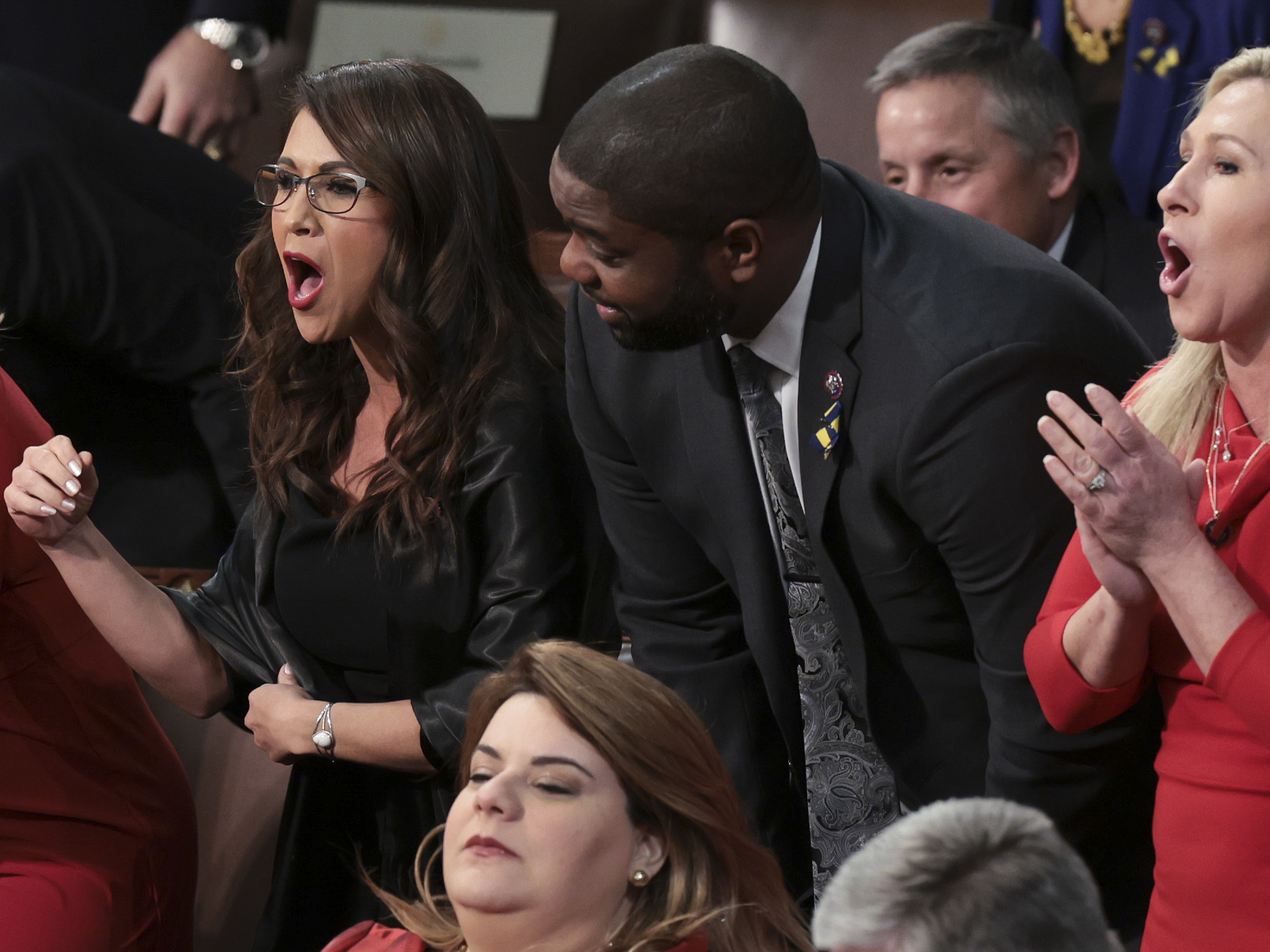 caption: Rep. Lauren Boebert, R-Colo. (left), and Rep. Marjorie Taylor Greene, R-Ga., stand with fellow lawmakers as they listen to President Biden's State of the Union address.