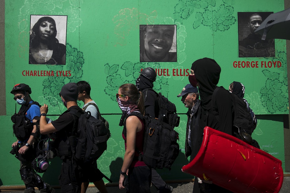 caption: Protesters and medics march along a mural with images of Charleena Lyles, Manuel Ellis and George Floyd during a Defund The Police march from the King County Juvenile Detention Center to Seattle City Hall on Wednesday August 5, 2020, in Seattle. 