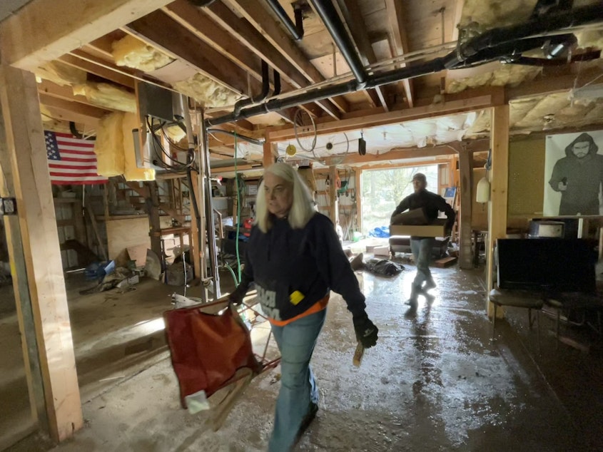 caption: Beth Easterday and AJ Van Dyke haul trash out of a the flooded shop of a friend who died back in May.