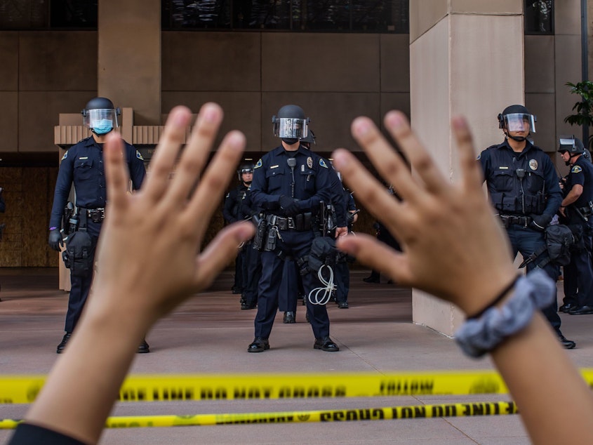 caption: A demonstrator holds her hands up while she kneels in front of the Police at the Anaheim City Hall on June 1, 2020 in Anaheim, California. Reform pressures have many cops leaving the job.
