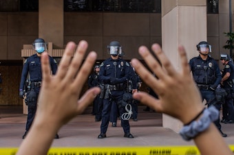 caption: A demonstrator holds her hands up while she kneels in front of the Police at the Anaheim City Hall on June 1, 2020 in Anaheim, California. Reform pressures have many cops leaving the job.