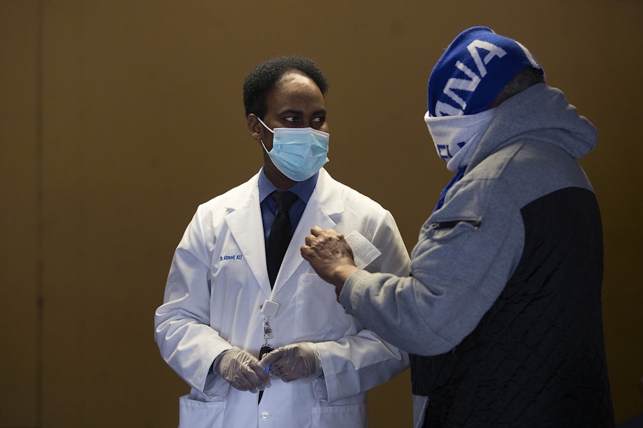 caption: Dr. Ahmed Ali, Executive Director of the Somali Health Board, left, talks with a community member who is set to receive their first dose of the Moderna Covid-19 vaccine, on Wednesday, February 3, 2021, at the Brighton Apartments complex on Rainier Avenue South in Seattle. The Othello Station Pharmacy provided 100 doses of the vaccine for seniors at the clinic.