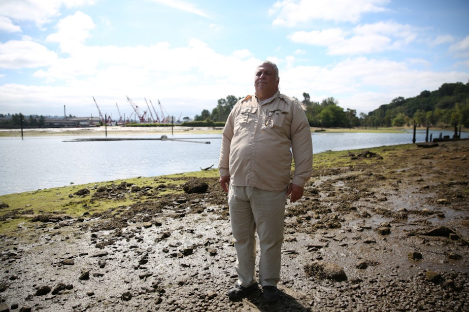 caption: James Rasmussen, director of the Duwamish River Cleanup Coalition and member of the Duwamish Tribe, stands on the bank of the river inside Seattle's Herring's House Park.