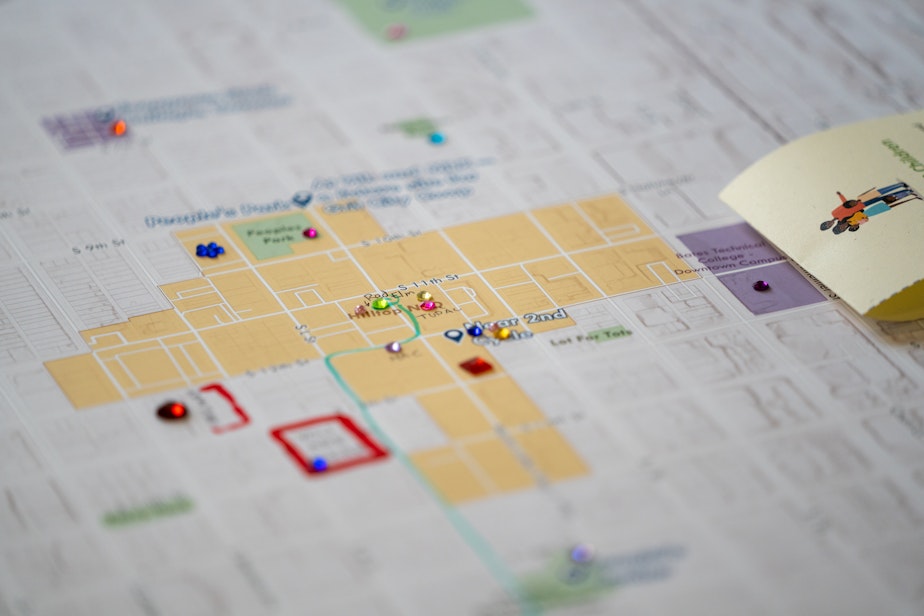 caption: A map plotting out a location for a new library in the Hilltop neighborhood. The map has lines from markers and plastic gemstones along frequented streets and areas.