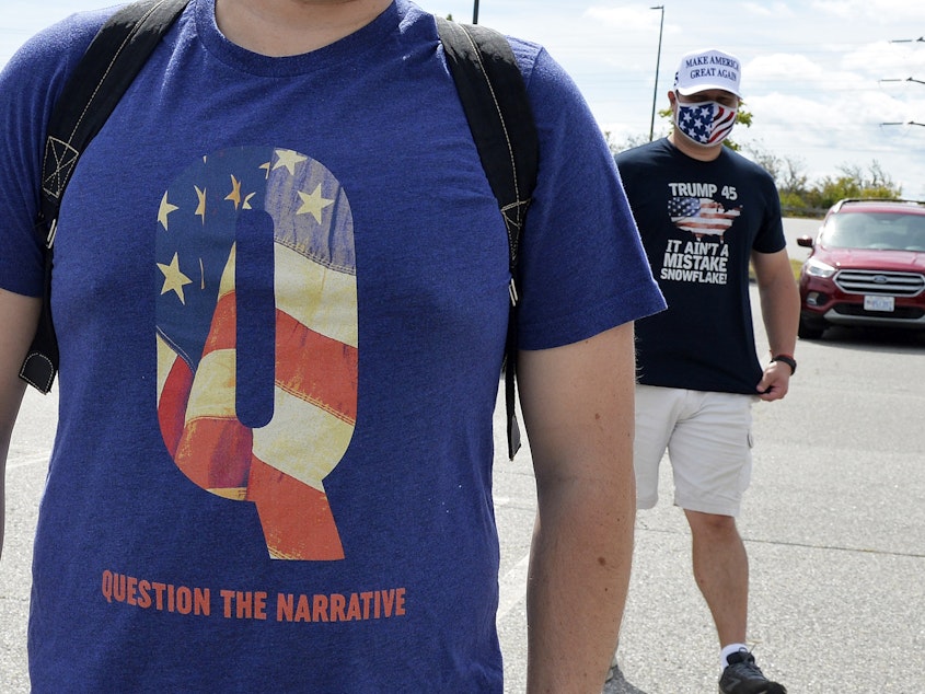 caption: A man wears a QAnon shirt while boarding a shuttle bus in Londonderry, N.H., on Aug. 28, 2020.