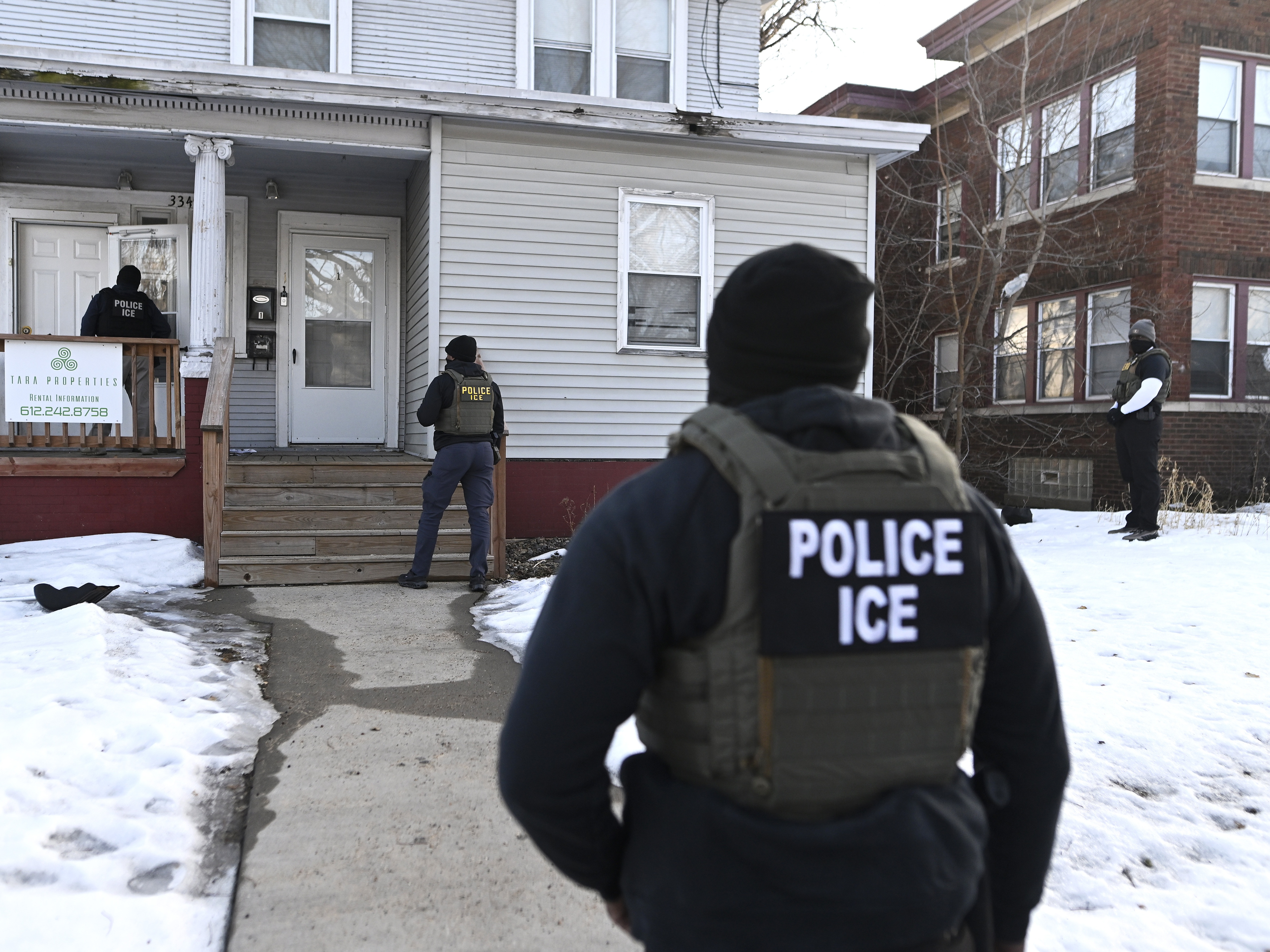 caption: ICE agents approach a house before detaining two people on Jan. 13 in Minneapolis.
