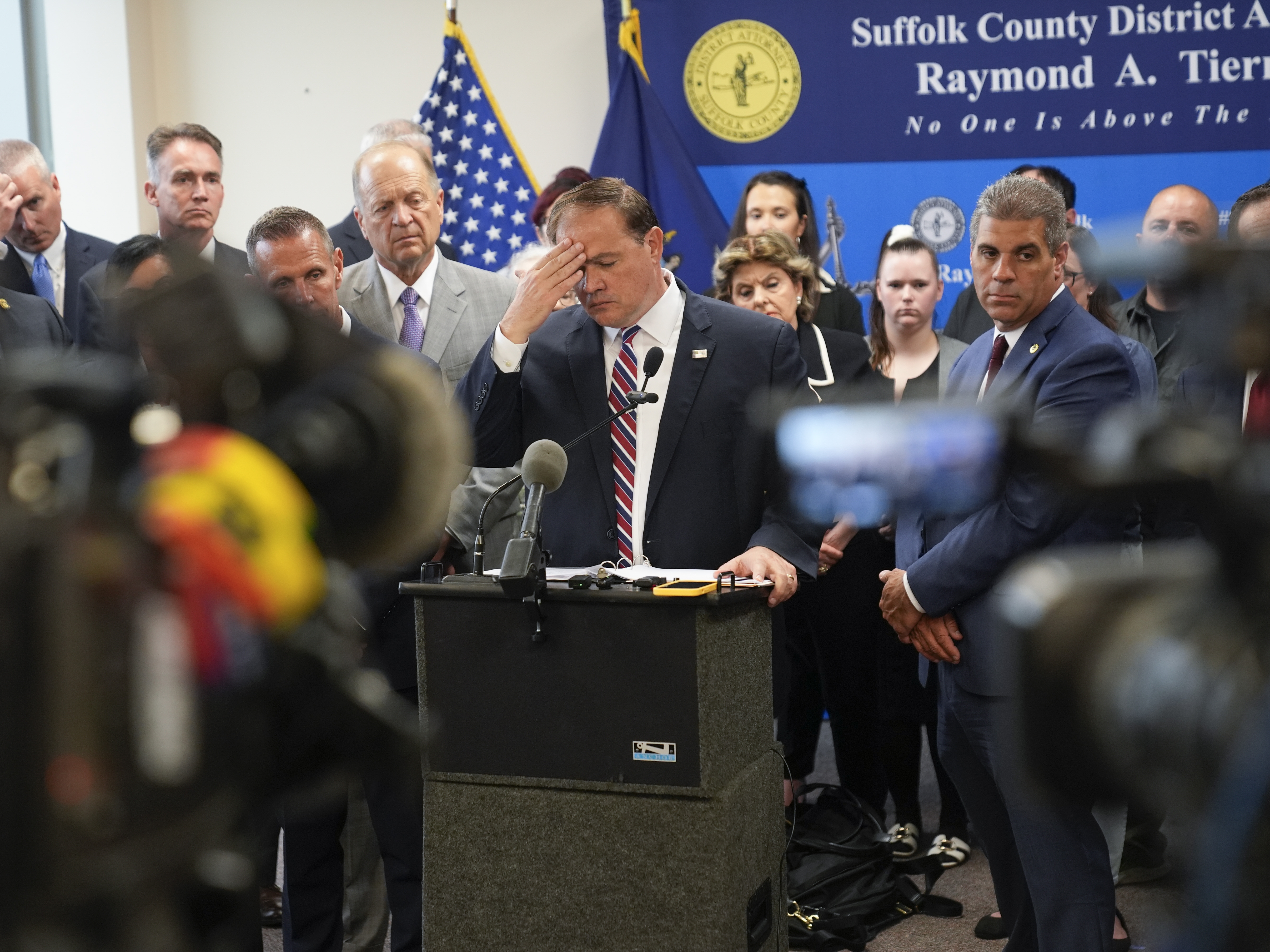 caption: Surrounded by law enforcement, victims' families, attorneys and others, Suffolk County District Attorney Raymond Tierney pauses during a news conference in Riverhead, N.Y., on Thursday.