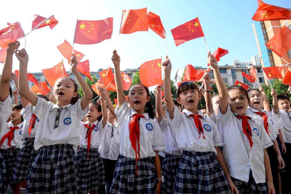 caption: Elementary school students waving national flags as they sing a patriotic song on the first day of the new semester in Handan in China's northern Hebei province. (STR/AFP via Getty Images)