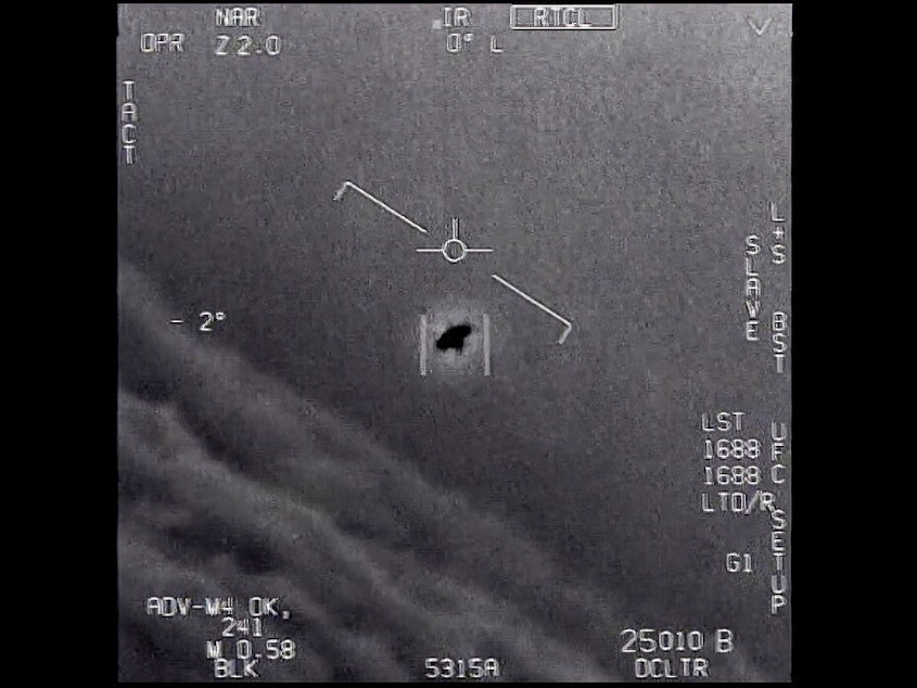 caption: In this image from 2015 video provided by the Department of Defense, an unexplained object is seen as it is tracked soaring high along the clouds, traveling against the wind.