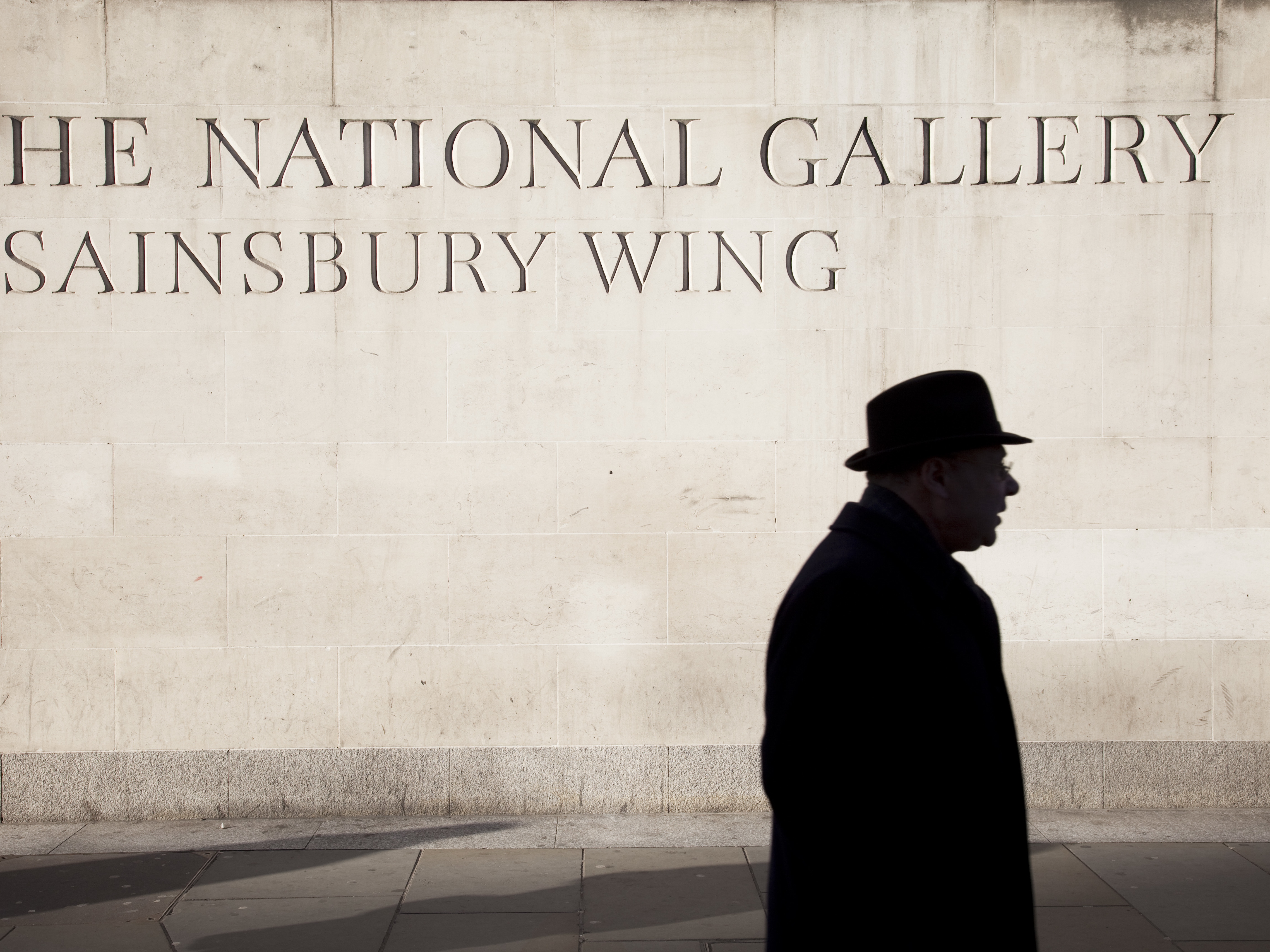 caption: A person walks by the Sainsbury Wing of the National Gallery, London.