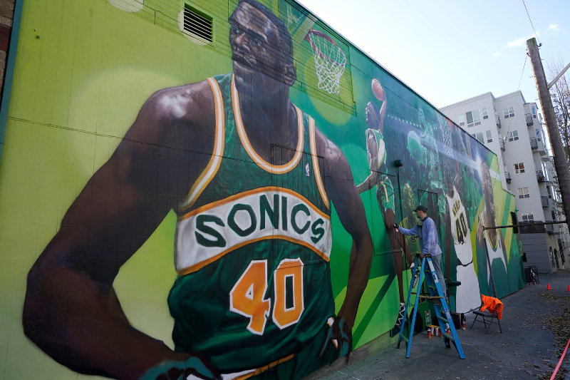 caption: An artist who goes by the name "Weirdo" puts the finishing touches on a giant mural on an outside wall of Shawn Kemp's Cannabis, the marijuana dispensary owned by Shawn Kemp, a former NBA basketball player for the Seattle SuperSonics and several other teams, and other business partners, Friday, Oct. 30, 2020, prior to the store's grand opening in downtown Seattle. 