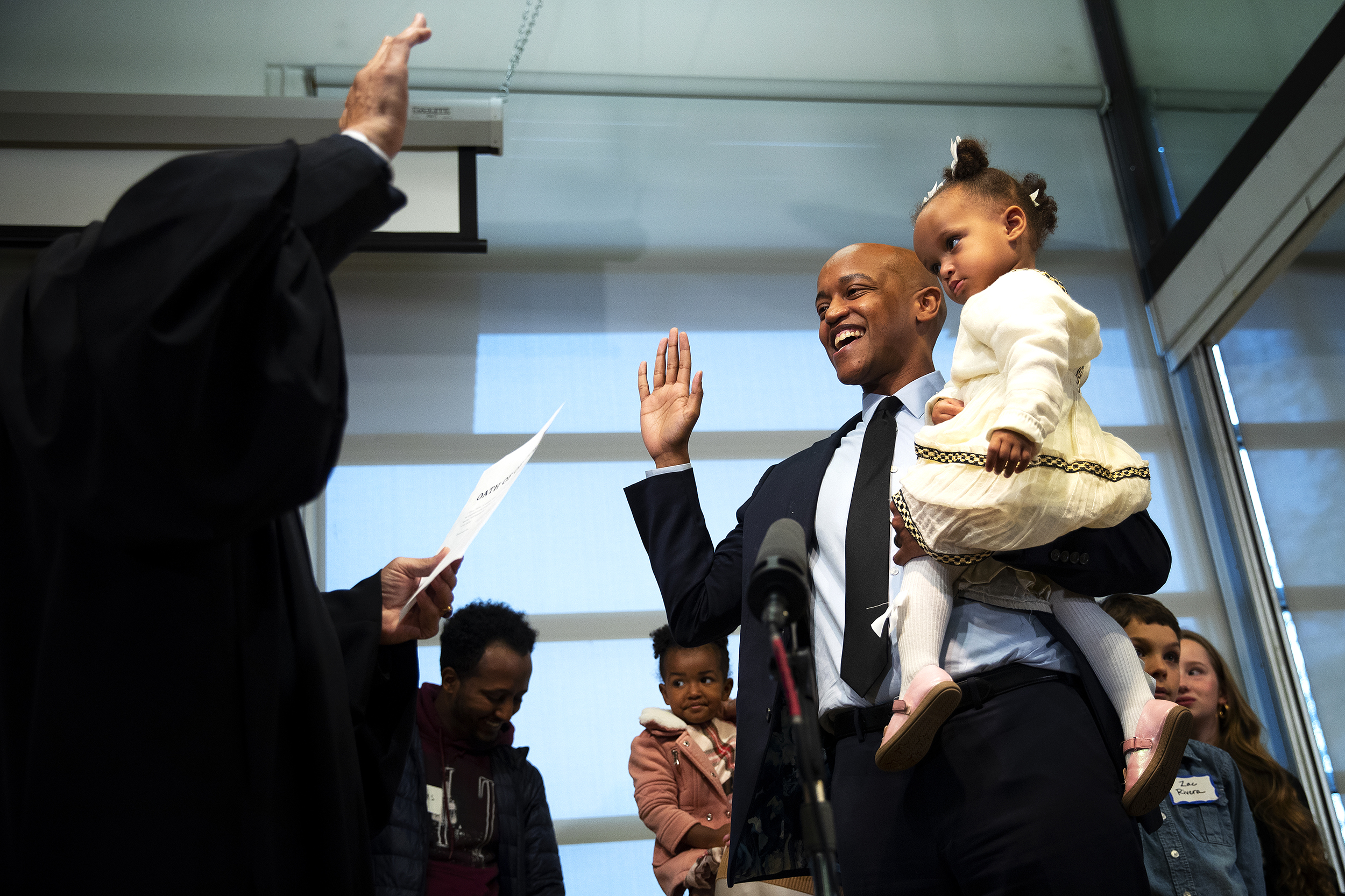 caption: Executive-elect Girmay Zahilay smiles while holding his daughter, Jazzy, as he's sworn in by Judge Richard Jones as King County executive during a community ceremony on Tuesday, Nov. 25, 2025, at the New Holly Gathering Hall. 