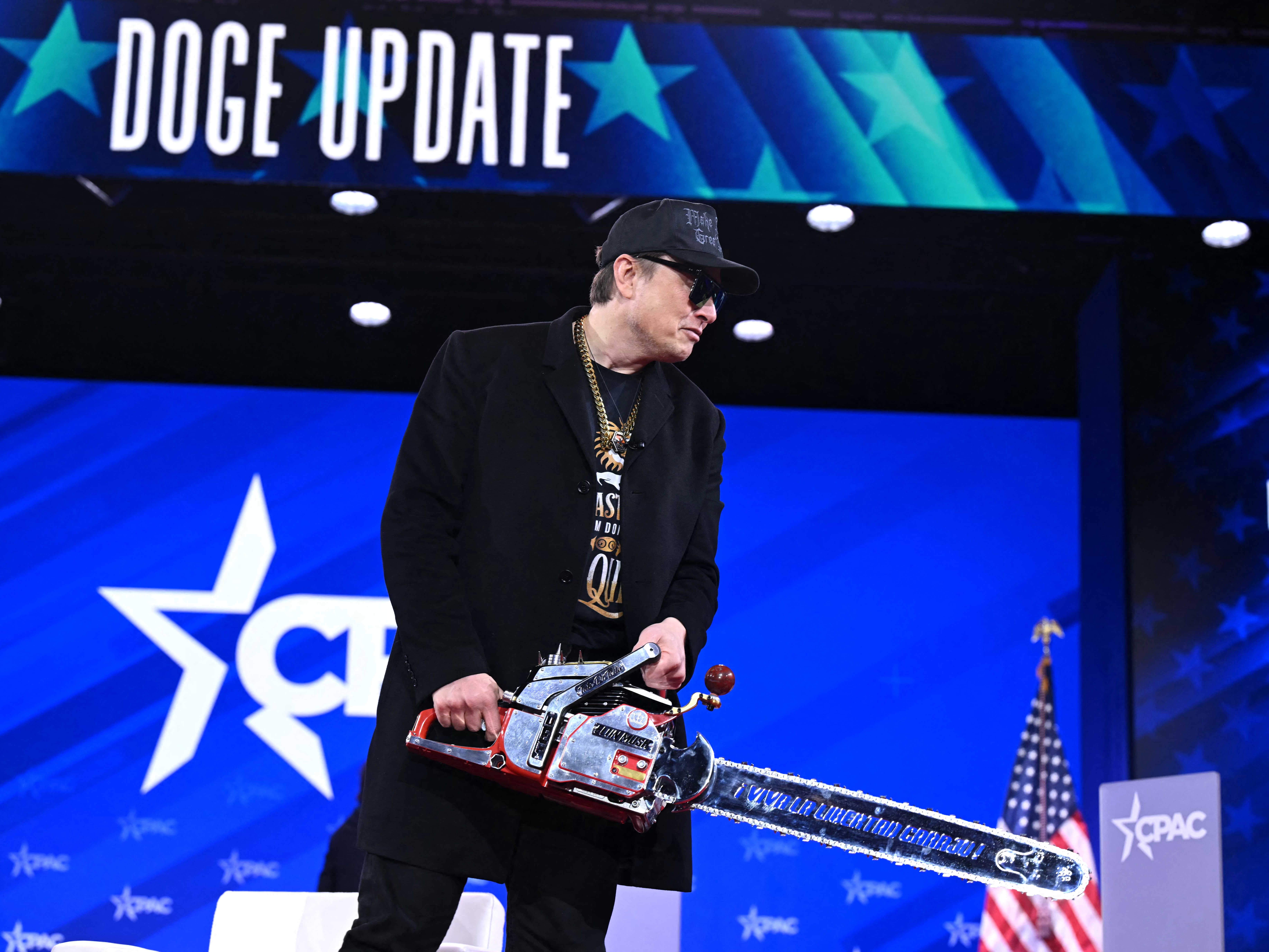 caption: Earlier this year, Elon Musk wielded what he called a "chainsaw for bureaucracy" during the annual Conservative Political Action Conference (CPAC) in Oxon Hill, Maryland, on February 20, 2025. While Musk no longer leads DOGE, the idea of trimming the federal government remains.