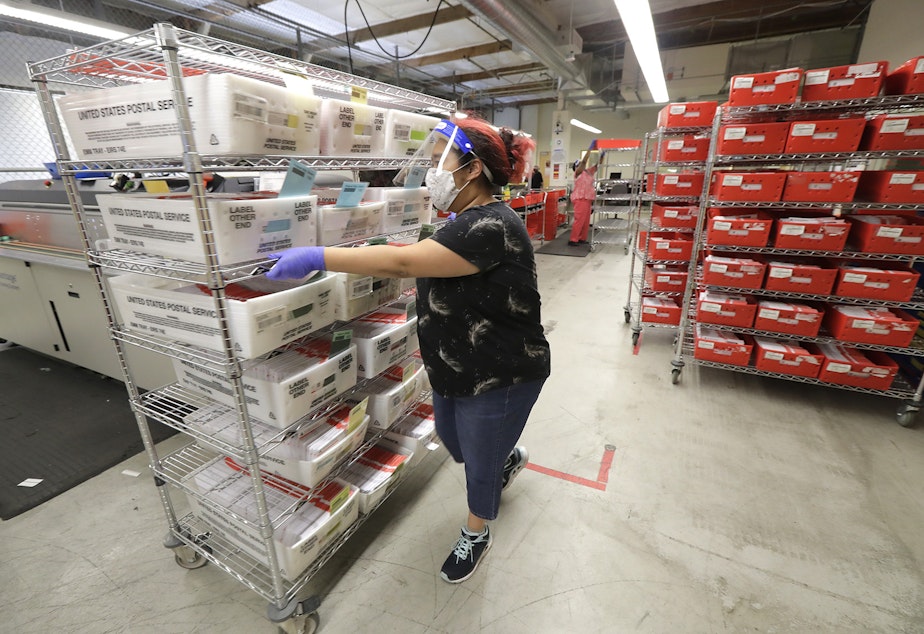 caption: A worker moves a cart of ballots that were either mailed in or dropped off at collection boxes from Tuesday's primary election, Wednesday, Aug. 5, 2020, at the King County Elections headquarters in Renton, Wash., south of Seattle. Washington.