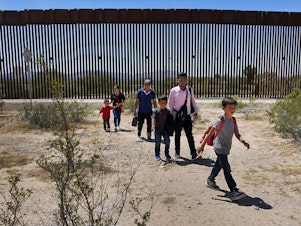 caption: A family of five who said they were from Guatemala and a man in a pink shirt from Peru walk through the desert after crossing in the Tucson Sector of the U.S.-Mexico border last month.