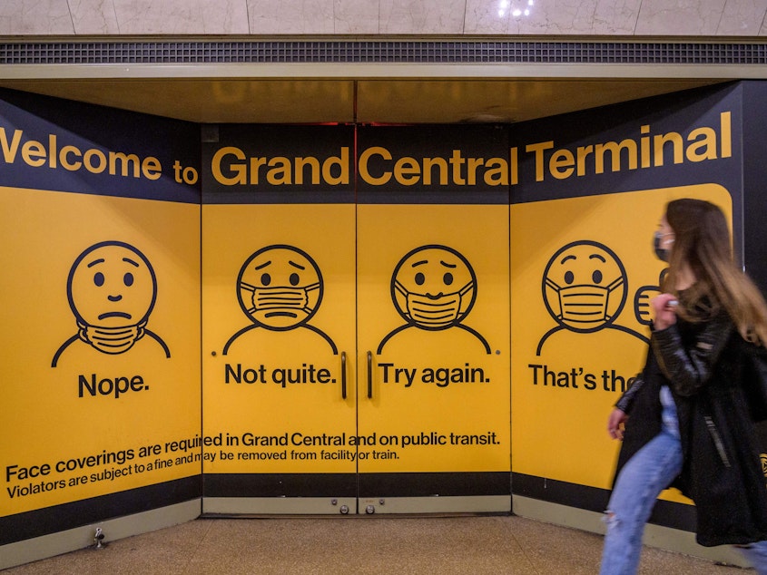 caption: A woman walks past posters explaining mask requirements at Grand Central Terminal train station in New York City on Wednesday. Rules requiring masks on transit are unchanged by the Centers for Disease Control and Prevention's updated mask guidance for fully vaccinated people.