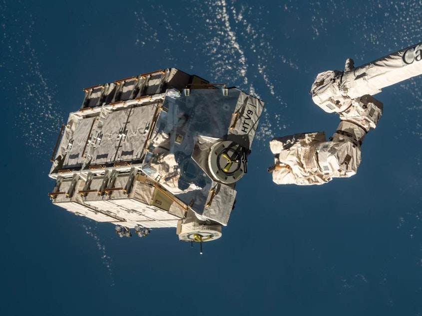 caption: A robotic arm at the International Space Station is seen releasing a pallet packed with batteries in 2021. NASA says a metal alloy stanchion from that flight equipment is what landed in a Florida home.
