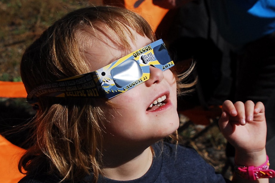 caption: "A supervised young child safely viewing the sun with solar eclipse glasses"