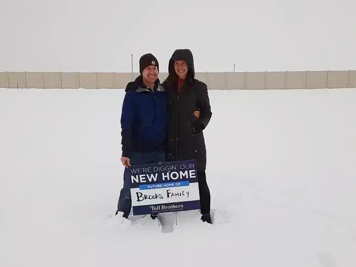 caption: Ari and TR Brooks stood on the land where their new home would be built the day they agreed to buy it back in February of 2021. But the home is still not completed and mortgage rates have risen dramatically.