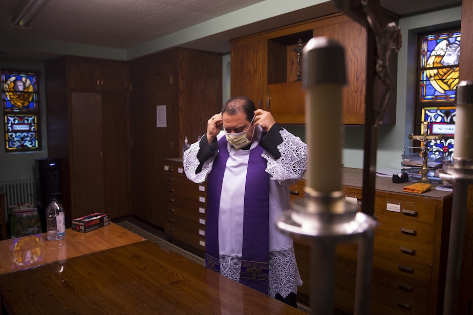 caption: Father Jose Alvarez puts on a mask before walk and drive through confessions on Friday, April 24, 2020, at Holy Family Roman Catholic Church in White Center. 