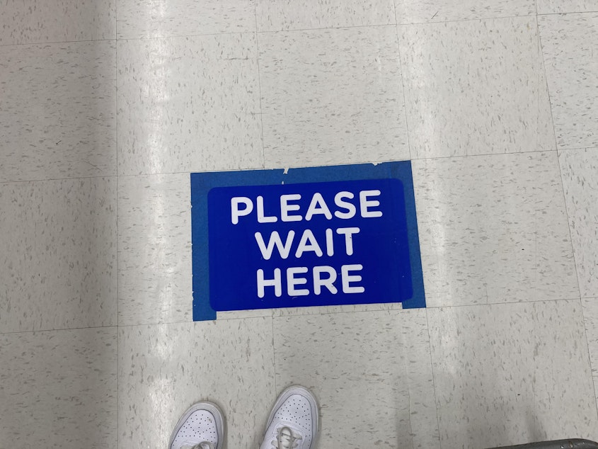 caption: The ‘Please Wait’ signs are plastered on the floors of each of the eleven checkout stands in the store. 