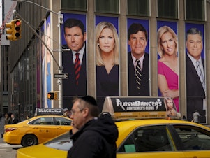 caption: Posters bearing the images of Bret Baier, Martha MacCallum, Tucker Carlson, Laura Ingraham, and Sean Hannity, from left, adorn the front of Fox Corp.'s headquarters in New York City. The stars' panic as viewers fled after the 2020 elections has become a core element of a $1.6 billion defamation suit against Fox.