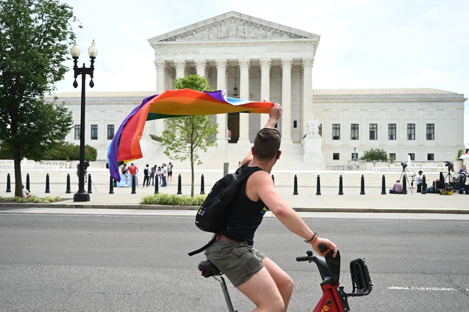 caption: A man waves a rainbow flag as he rides by the US Supreme Court that released a decision that says federal law protects LGBTQ workers from discrimination on June 15, 2020 in Washington,DC. (JIM WATSON/AFP via Getty Images)