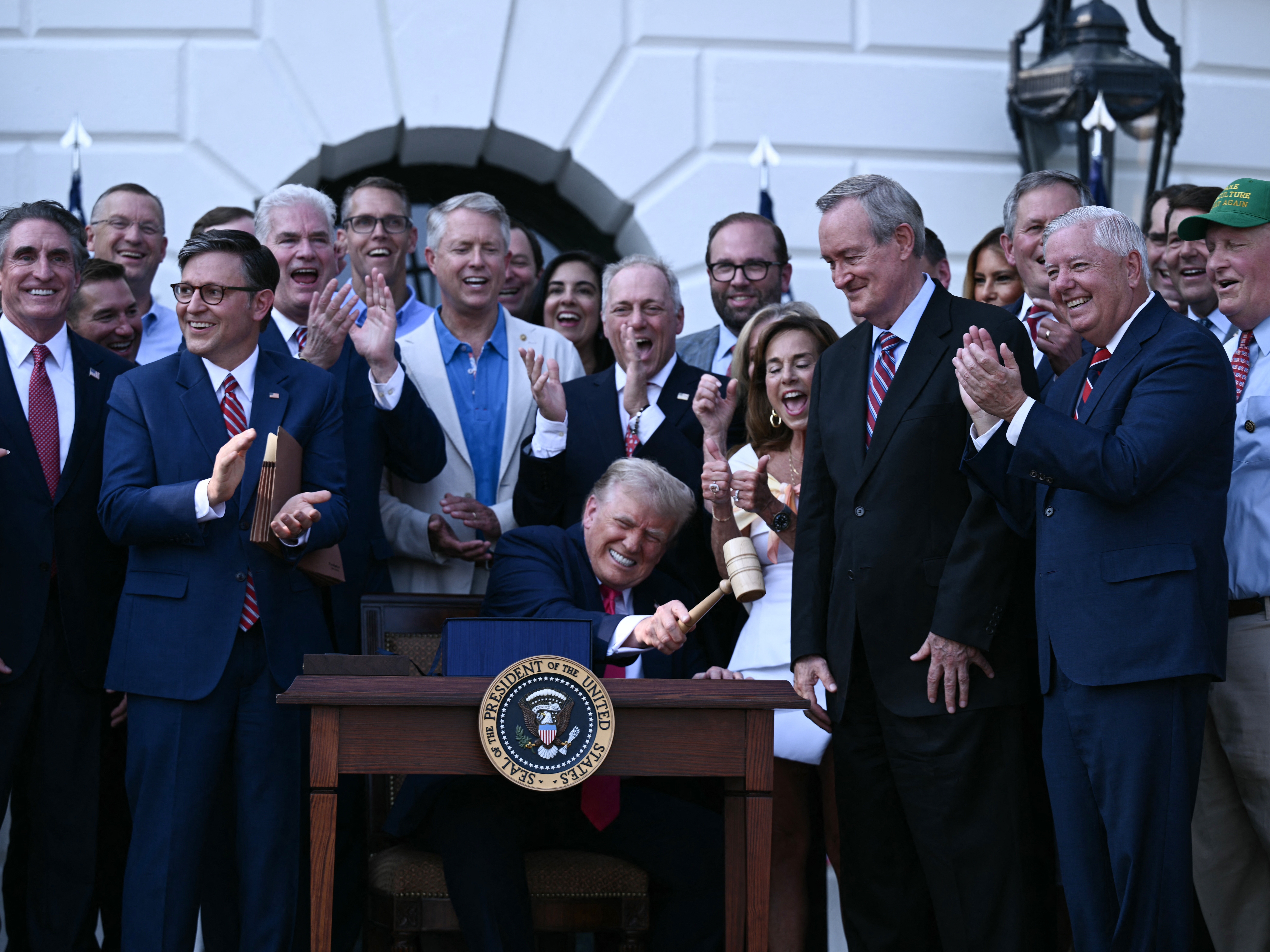 caption: President Trump bangs a gavel after signing the One Big Beautiful Bill Act at the White House on July 4.