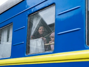 caption: A woman and her daughter take a train out of Lviv toward Poland in March, leaving her husband behind on the platform.