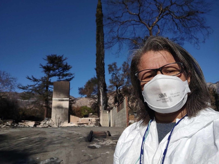 caption: KUOW Morning Edition host Angela King dons PPE in front of what remains of aunt’s home in Altadena.